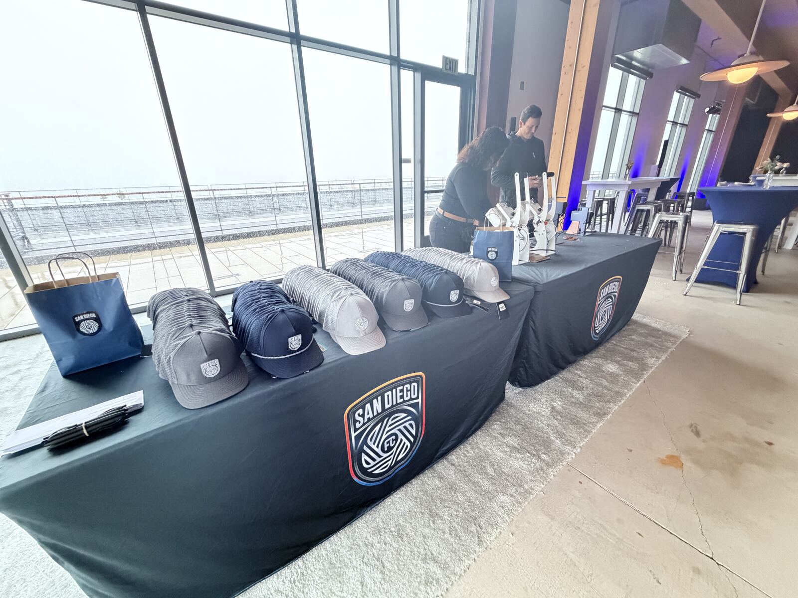 Event staff booth displaying branded hats and merchandise on a table with a San Diego Waves logo banner